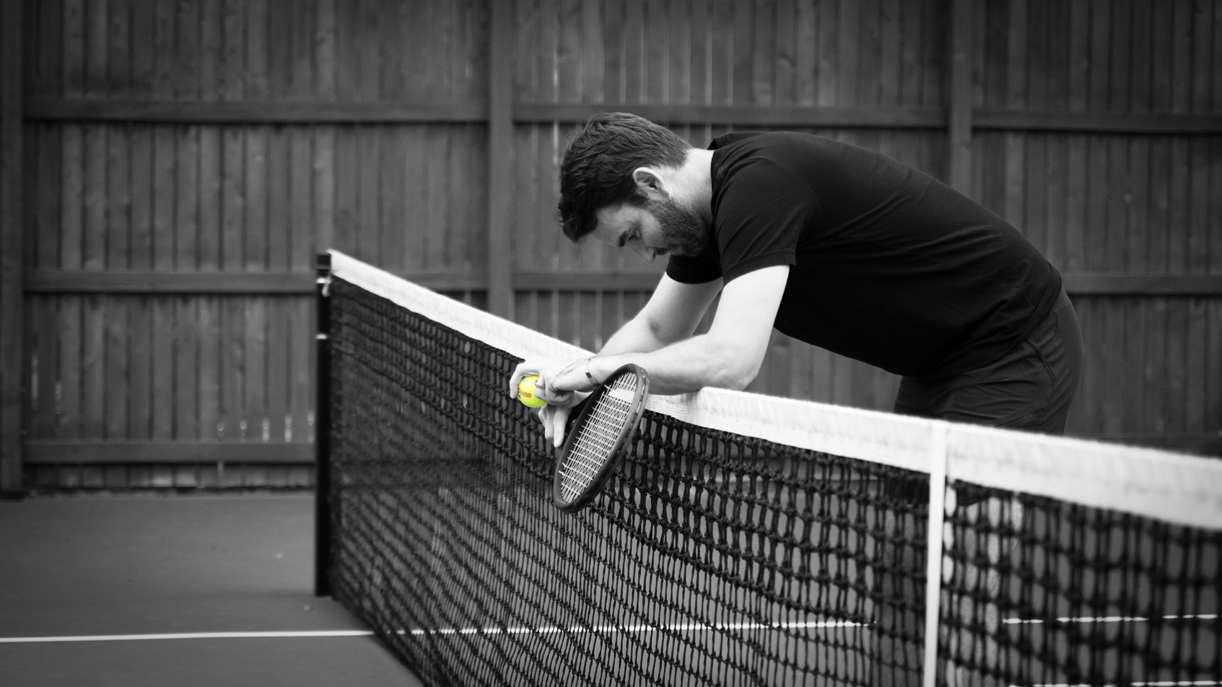 A player slumped over the net holding his racket and a tennis ball, experiencing discomfort.