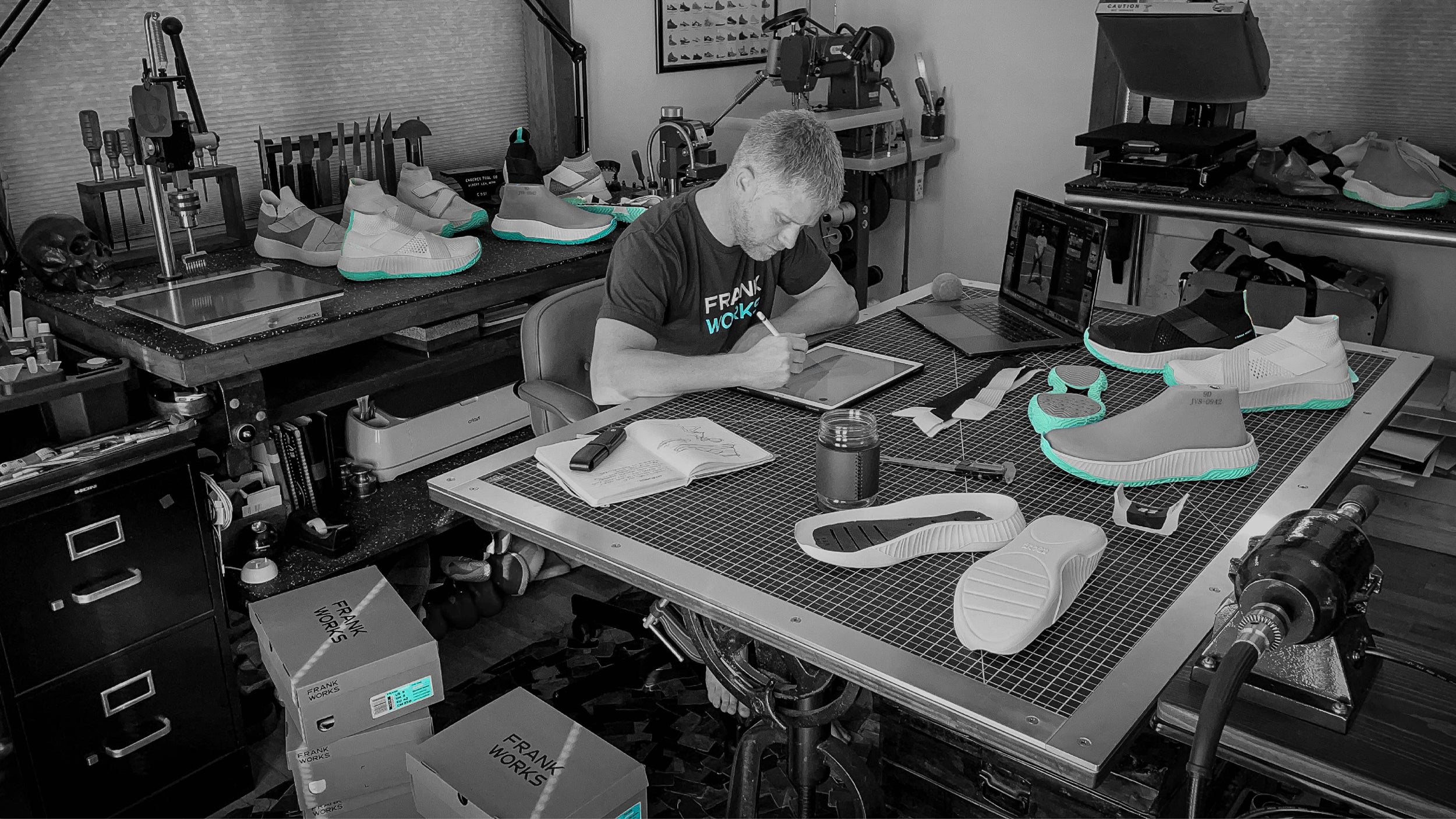 A black and white photo of Co-Founder Greg Newman in his workshop at his desk designing.