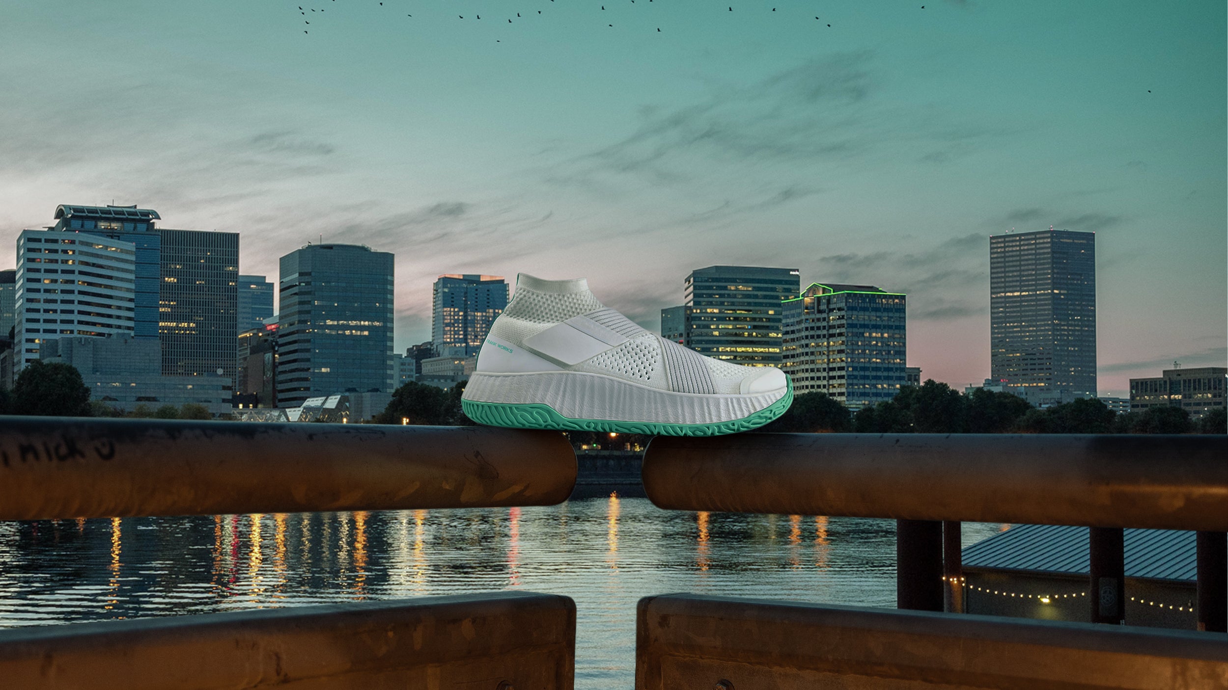 The right shoe of the white/white colorway of The One resting on a handrail with the Portland skyline in the background.